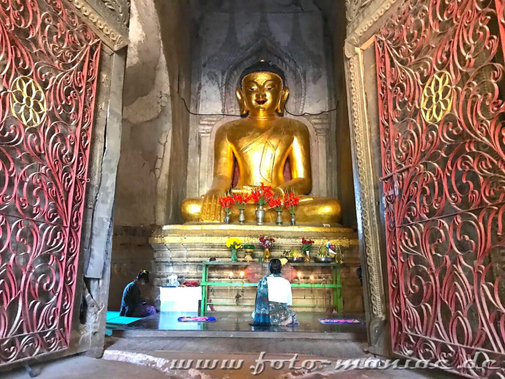 Zwei Betende knien vor einem goldenen Buddha
