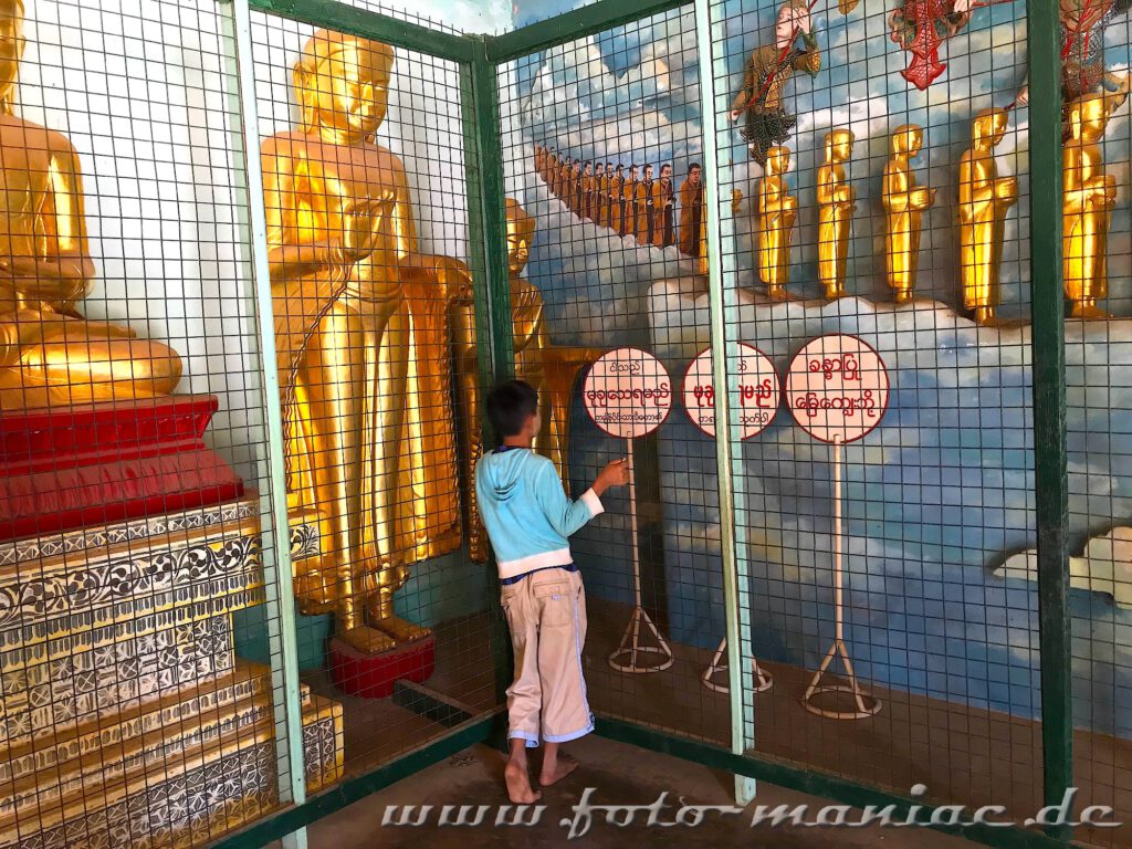 Ein Junge betrachtet die Buddhas hinter Gitter