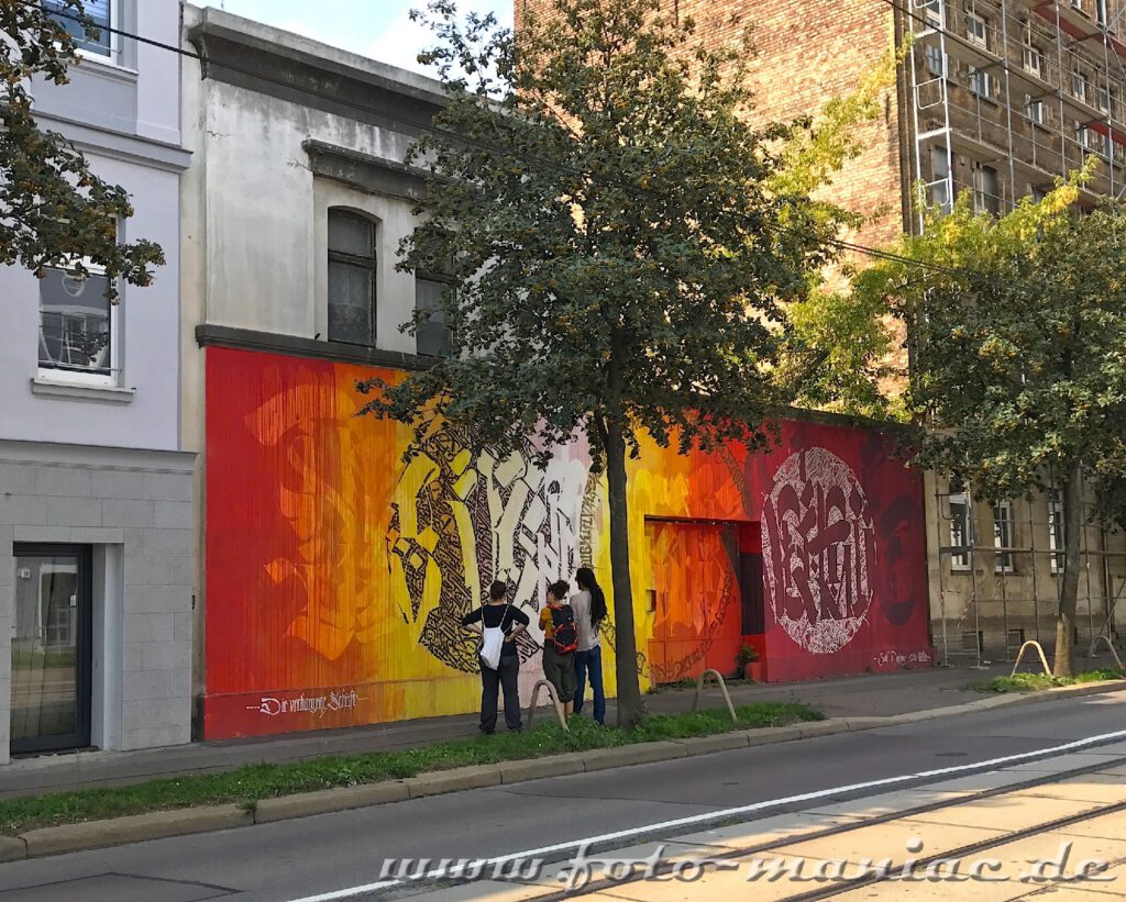 Drei junge Leute schauen sich ein Mauer-Graffito an