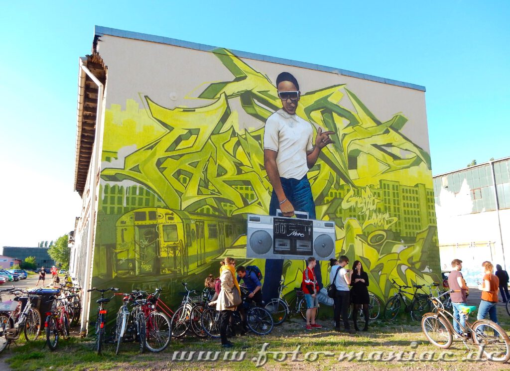Jugendliche unter einem Graffito, das einen Jungen mit Sonnenbrille und Radio zeigt