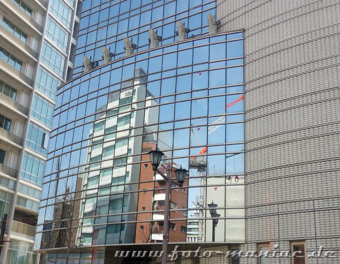 In einer Glasfassade spiegeln sich Gebäude