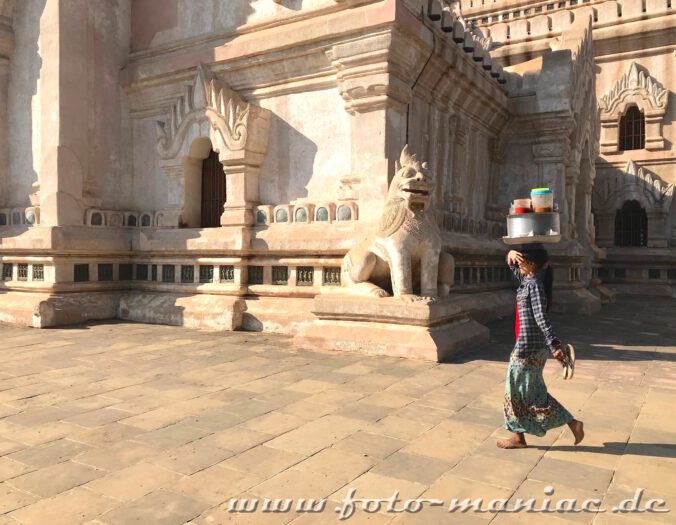 Einzigartige Tempelstadt Bagan - Frau mit Behältern auf dem Kopf schützt sich vor dem Ananda Tempel in der einzigartigen Tempelstadt Bagan mit der Hand vor der Sonne