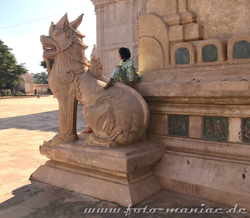 Einzigartige Tempelstadt Bagan - Mädchen sitzt vor dem Ananda Tempel auf einem steinernen Löwen