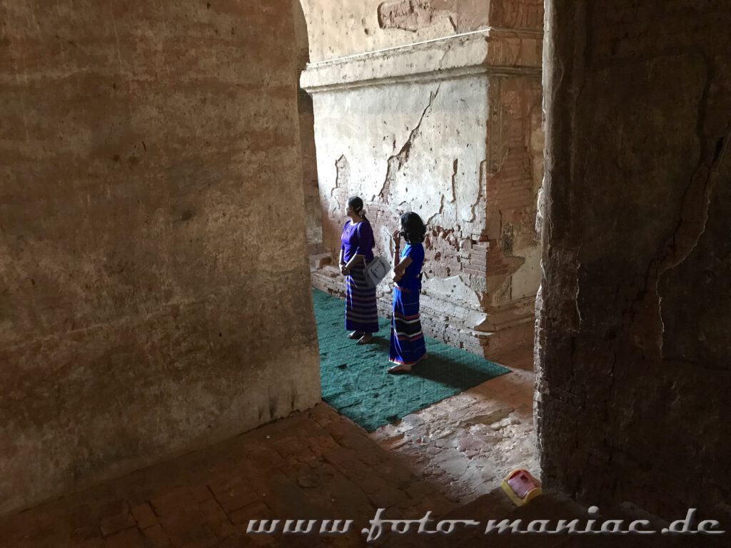 Zwei Frauen stehen zwischen hohen Mauern des Dhammayangyi Tempels