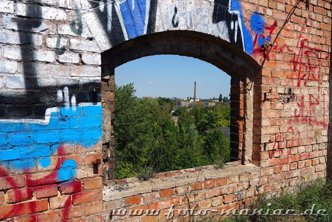 Durch einen Fensterdurchbruch geht der Blick von der verlassenen Spritfabrik in Halle zu einem Schornstein