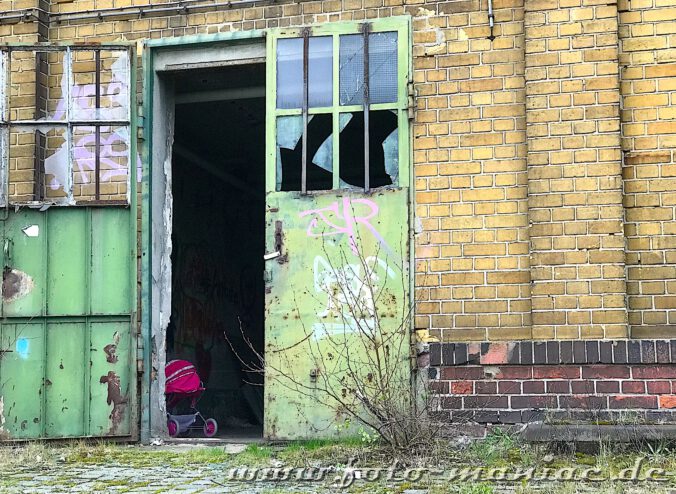 Hinter einer halb geöffneten Hallen-Tür steht ein roter Puppenwagen