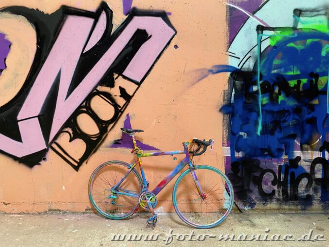 Mit bunten Farben besprühtes Rennrad vor Graffiti in Turnhalle