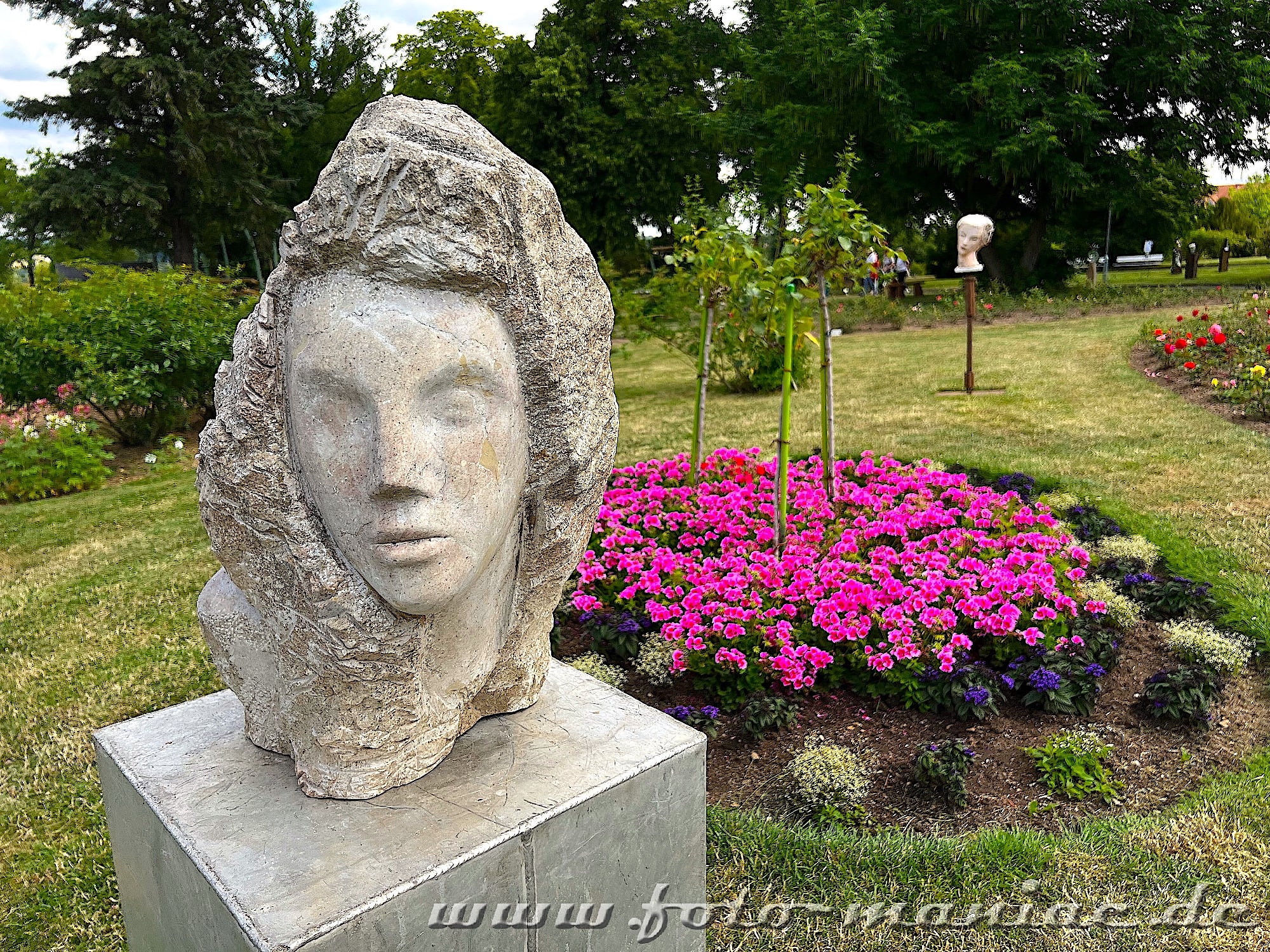 Ein Frauenkopf vor einem Blumenbeet gehört zur Ausstellung Kunst im Rosarium Sangerhausen