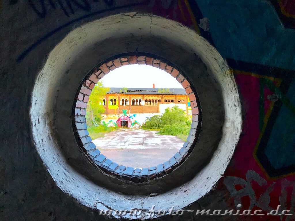 Blick durch eine kreisrunde Öffnung auf ein Gebäude des maroden Schlachthofs