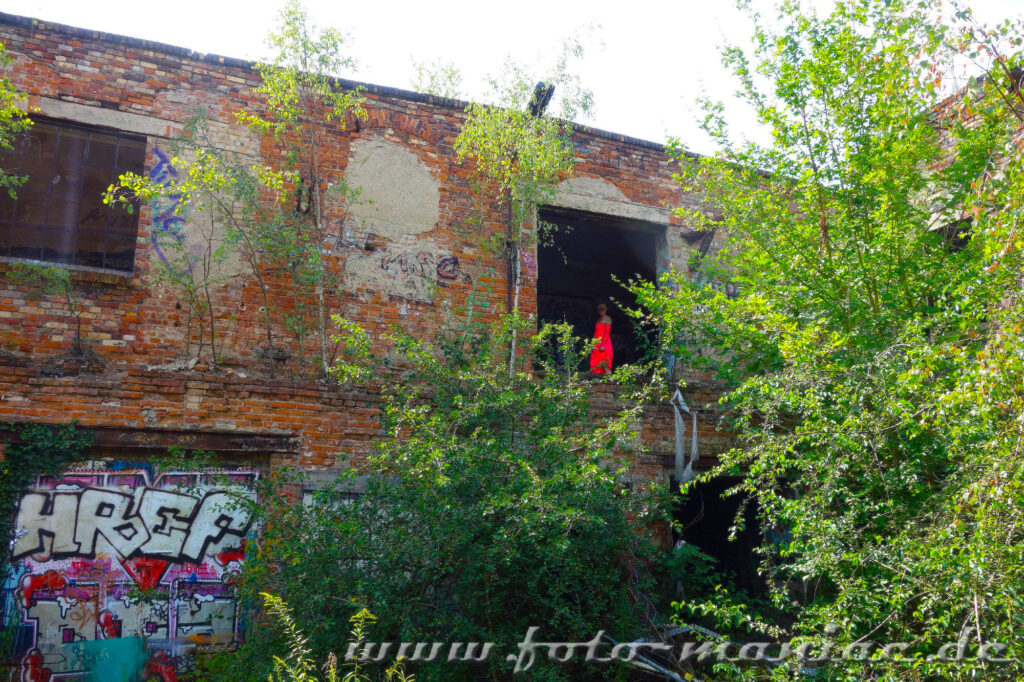 Frau im roten Kleid an einer Maueröffnung in der alten Papierfabrik in Halle