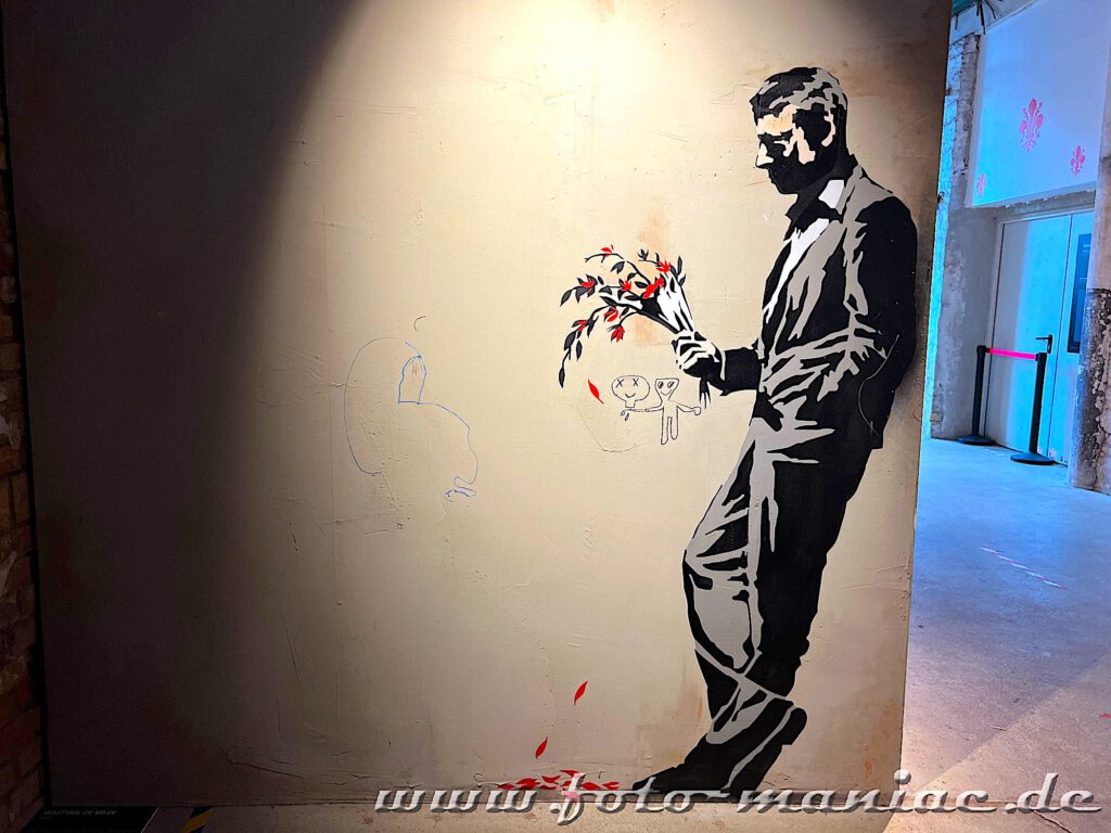 Banksy im Kunstkraftwerk Leipzig: Ein an die Wand gelehnter wartender Mann hält einen Blumenstrauß
