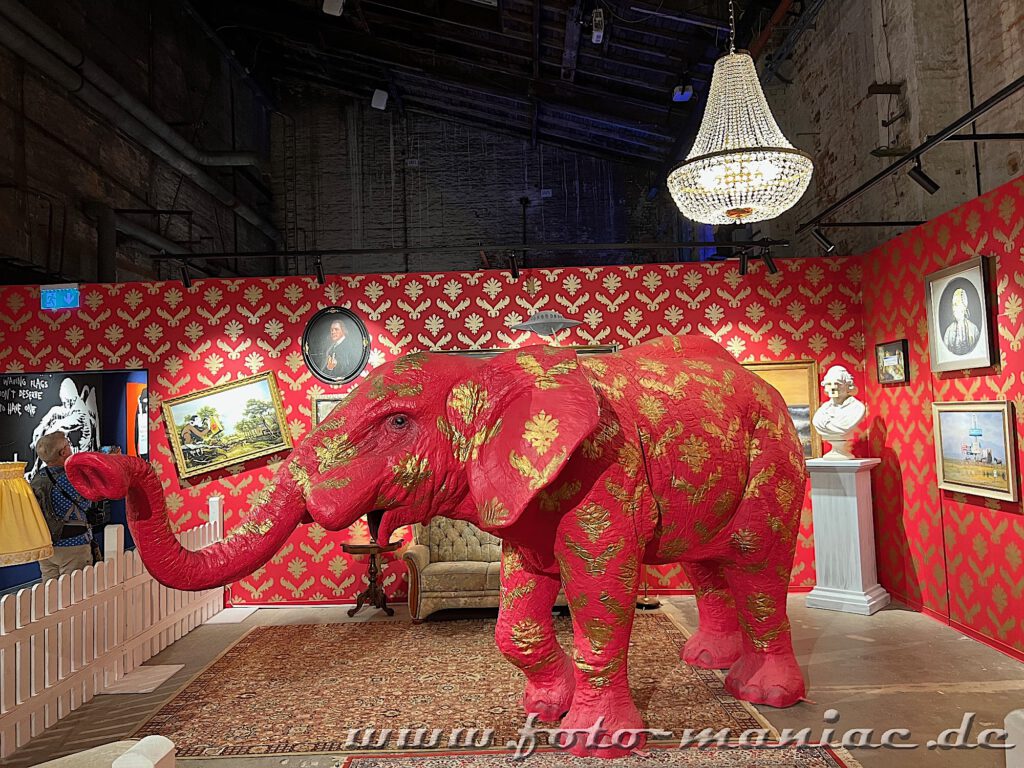 Rot-goldener Elefant in einem Zimmer mit rot-golden gemusterter Tapete