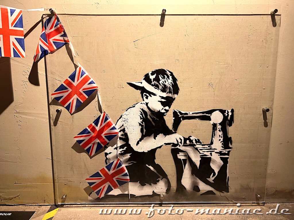 Banksy im Kunstkraftwerk Leipzig - Junge näht mit der Nähmaschine im Akkord englischen Fahnen