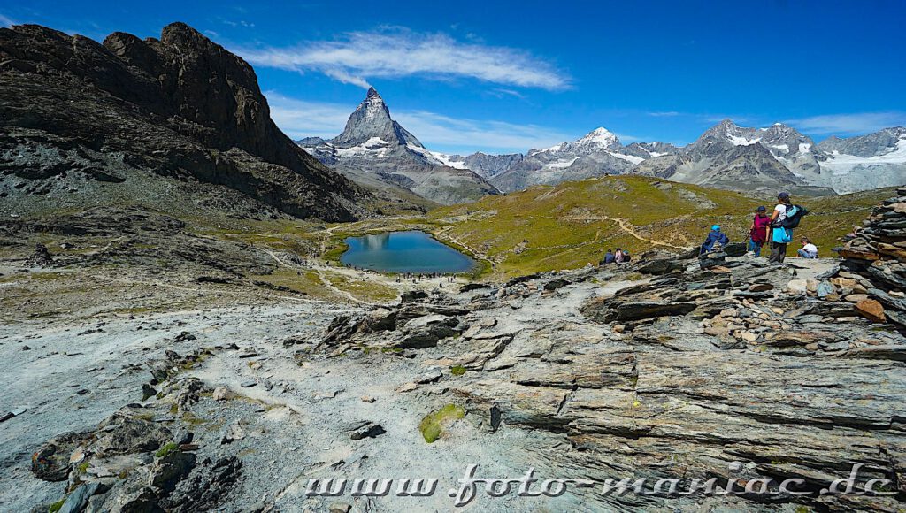 Kaiser von Zermatt: Wanderer schauen von oben auf den Riffelsee, auf dessen Oberfläche sich das Matterhorn spiegel