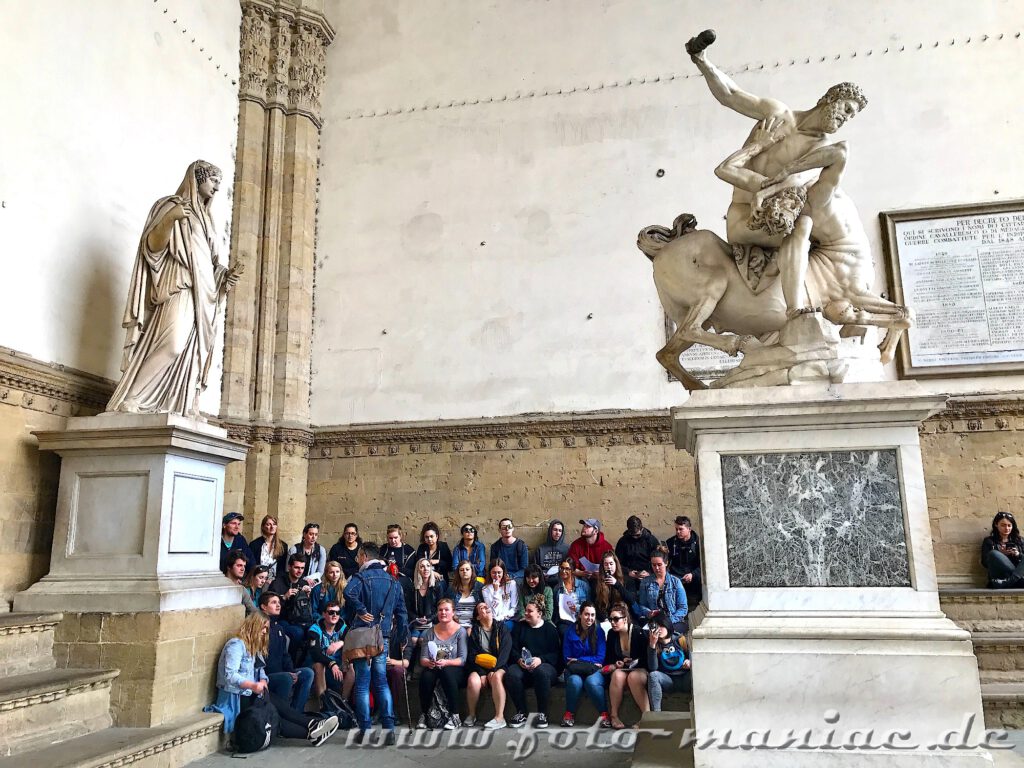 Kurzreise nach Florenz: Eine Touristengruppe sitzt auf der Loggia dei Lanzi zwischen historischen Skulpturen