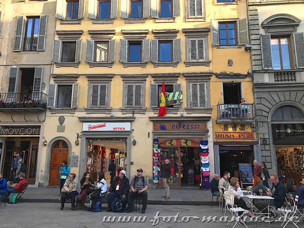 Menschen sitzen auf Bänken und Stühlen auf einer Straße in Florenz